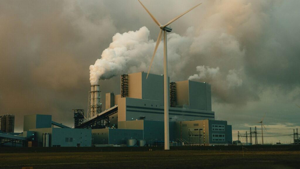 Industriële fabriek met windmolens en rookpluimen, beïnvloedt luchtkwaliteit in woonomgevingen.